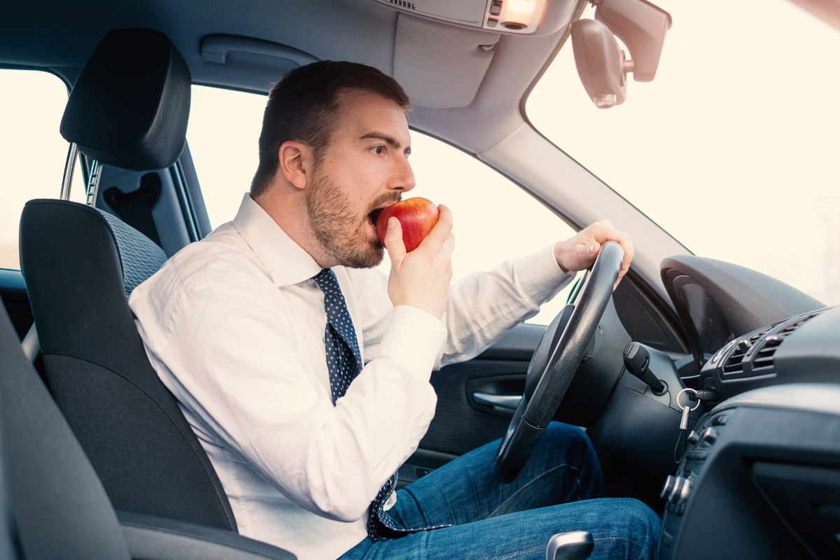 Même si la loi ne l'interdit pas formellement, si vous souhaitez boire et manger au volant, sachez que vous pouvez être verbalisé par les forces de l'ordre. Crédit photo : Shutterstock - Mondial de l'Auto 2022