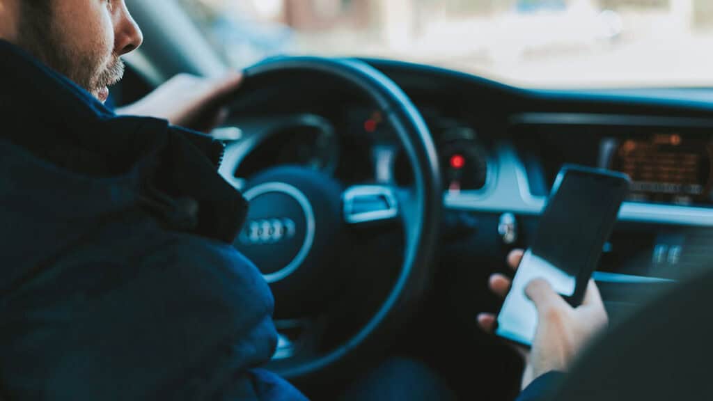 photo d'un homme au volant de sa voiture electrique avec son portable dans la main - applications pour voitures electriques - mondial de l'auto 2024