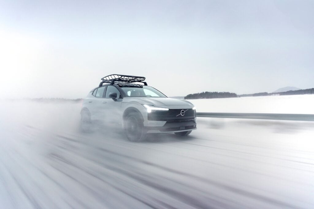 Volvo EX30 Cross Country dans la neige qui vole sur une route d'hiver en suéde